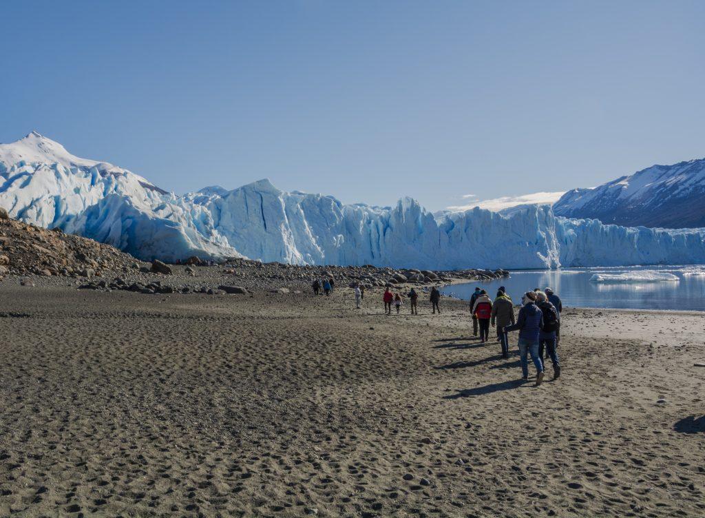Caminantes por la playa del lago frente al glaciar Perito Moreno