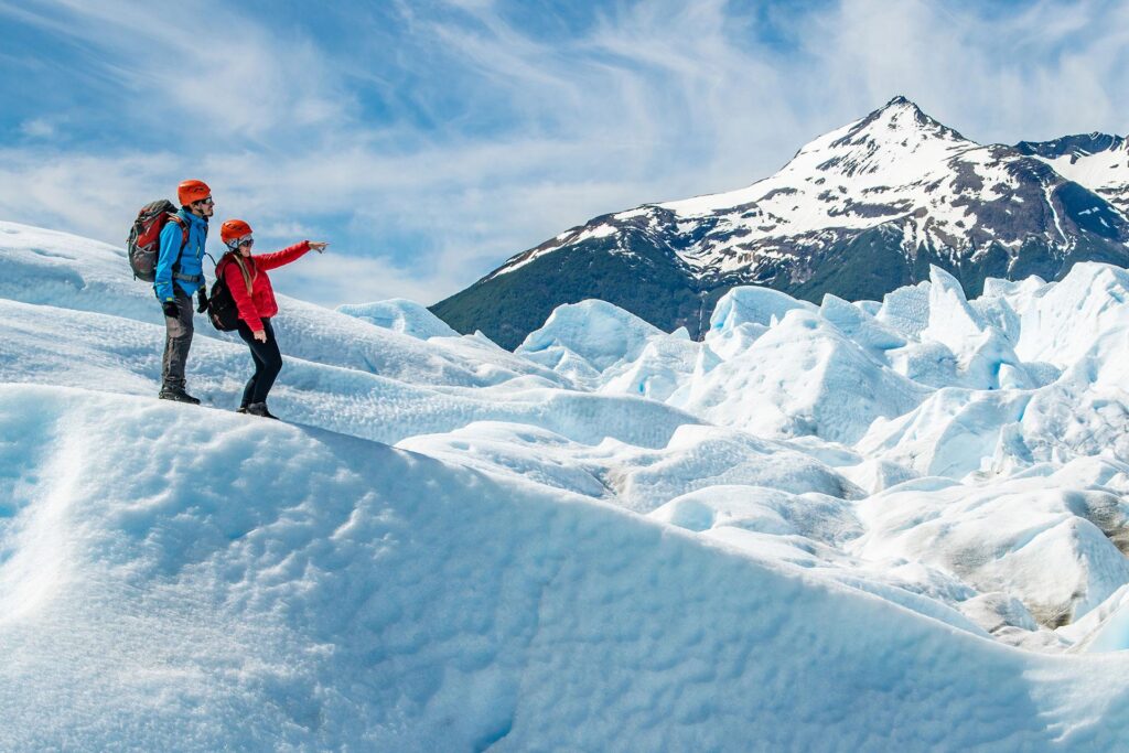Pareja de exploradores sobre el hielo del glaciar con montañas nevadas